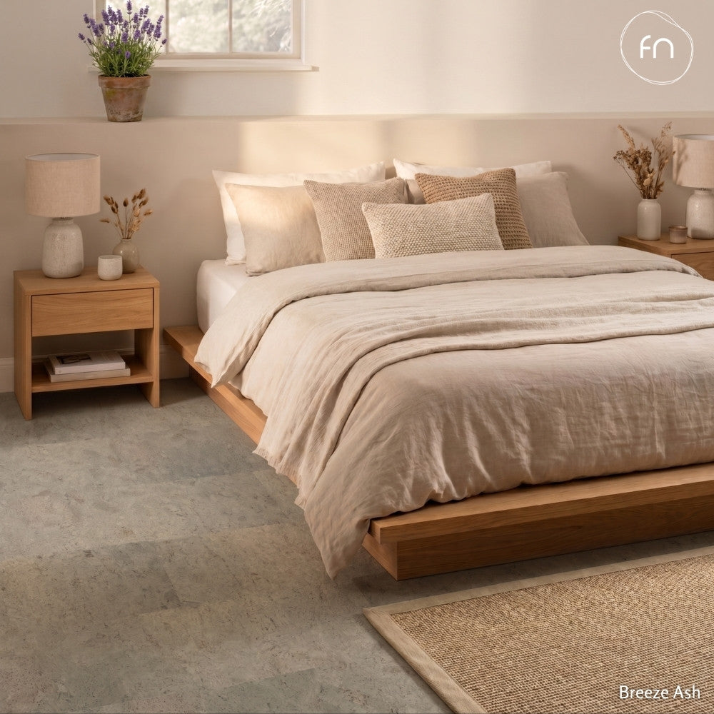 Neatly made bed with beige bedding in a bedroom setting, featuring wooden nightstands and grey cork flooring.