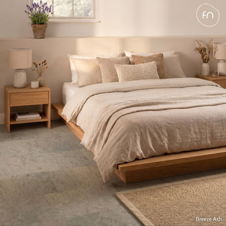 Neatly made bed with beige bedding in a bedroom setting, featuring wooden nightstands and grey cork flooring.