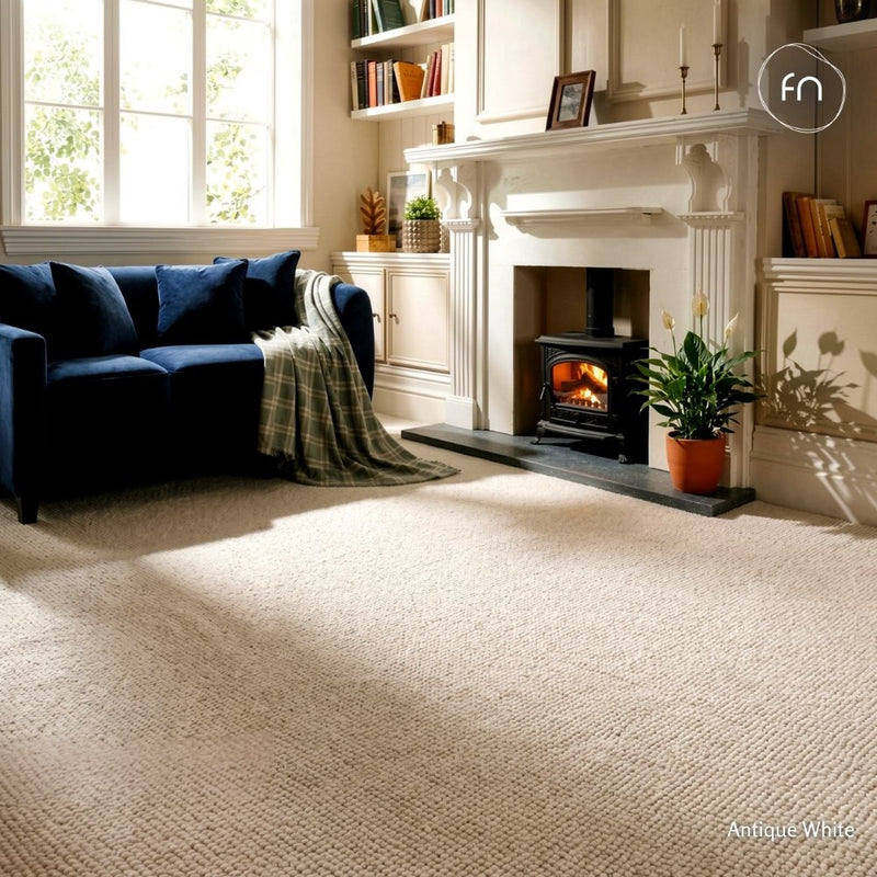 A loop pile wool carpet in an antique white or light beige tone, shown in a styled living room with a blue sofa, fireplace, and potted plant.