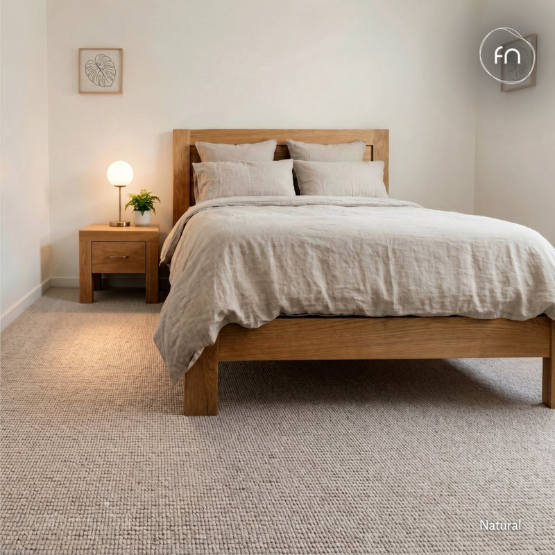 A natural wood platform bed with light beige linen bedding, styled in a minimalist bedroom with a matching wood nightstand, a lit table lamp, and chunky loop wool carpet.