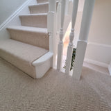 A beige herringbone-patterned carpet installed on a staircase and landing, with white wooden balusters and steps also covered in matching carpet.
