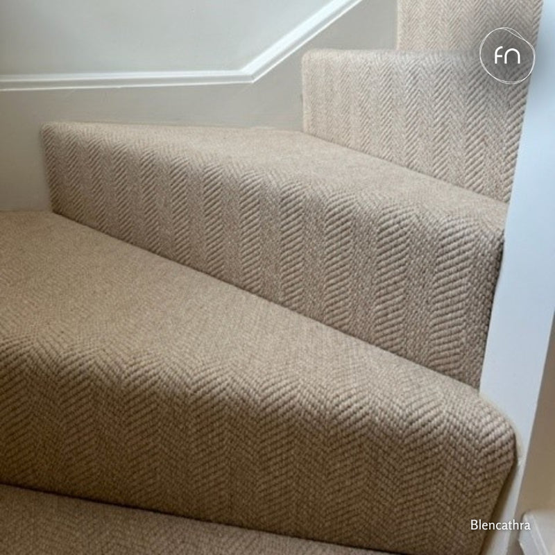 A close-up view of carpeted stairs with an undyed wool herringbone pattern.