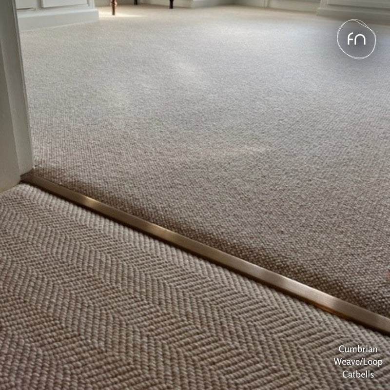Close-up of a carpeted interior doorway showing two colour matching carpet styles: a herringbone-patterned carpet in the foreground and a textured loop pile carpet in the background, divided by a metal threshold strip.