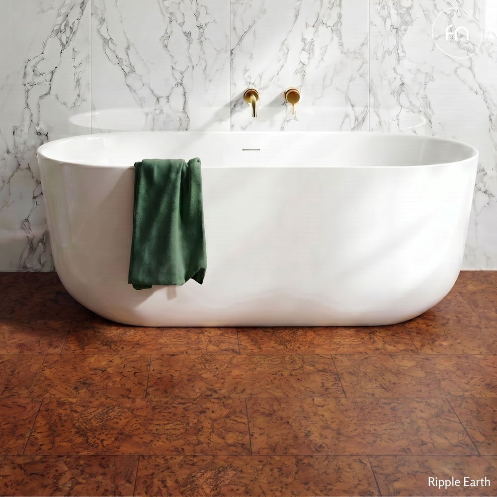 White freestanding bathtub with a green towel on a cork floor and against a marble wall.