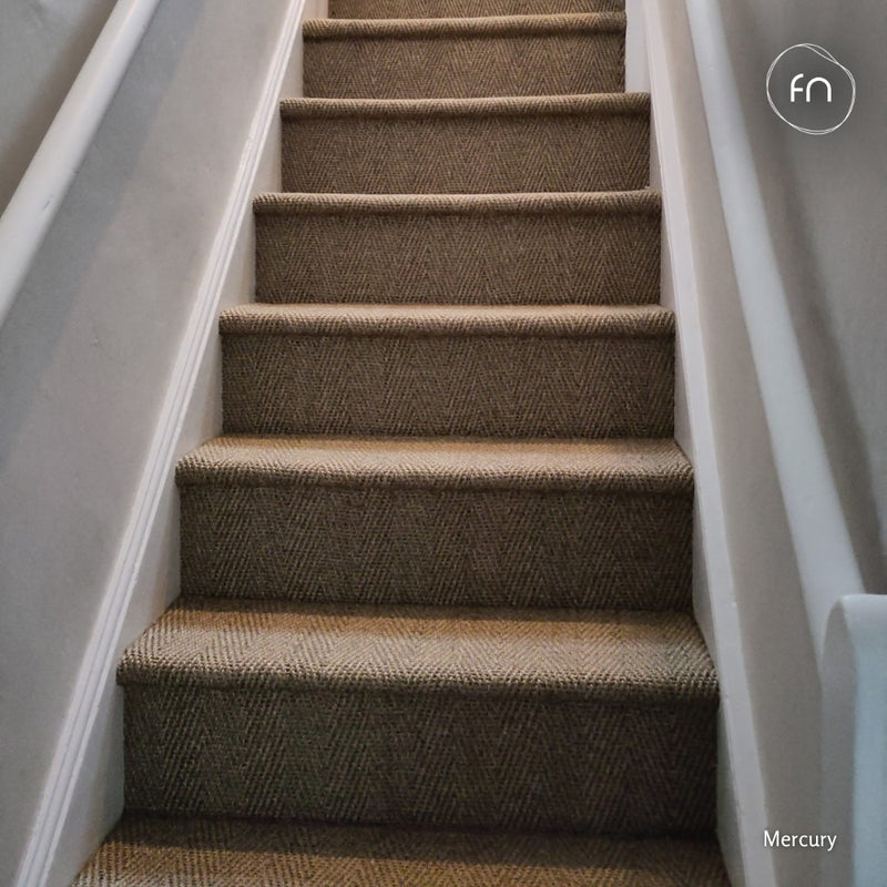 A carpeted staircase with textured brown and beige herringbone-patterned sisal carpeting, bordered by white walls and handrails.