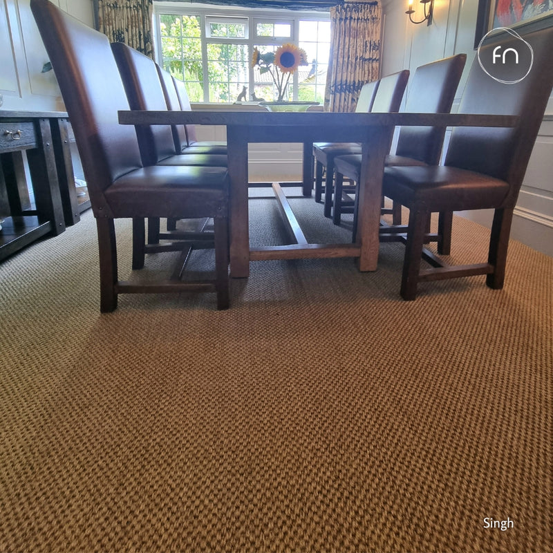 A dining room scene showing a dark wood dining table with six dark brown upholstered chairs, set on a textured golden sisal carpet in a home interior.